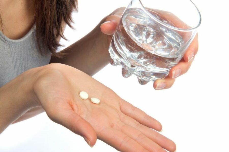 Таблетки и стакан с водой в руках